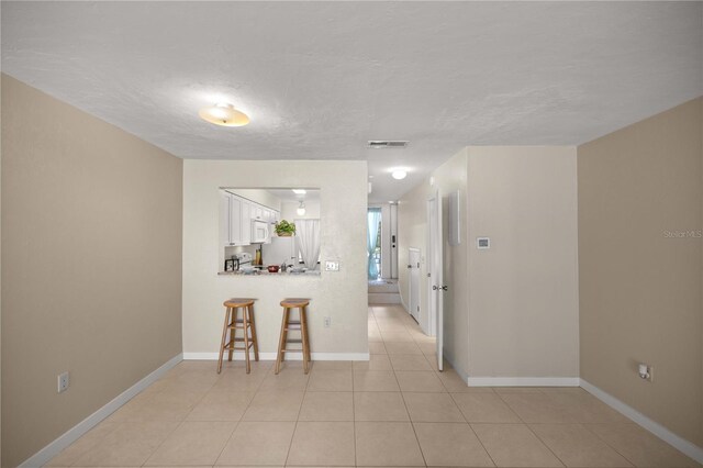 1428 SW 25th Pl, Gainesville, FL 32608 - kitchen with a breakfast bar area, white microwave, white cabinetry, a peninsula, and baseboards