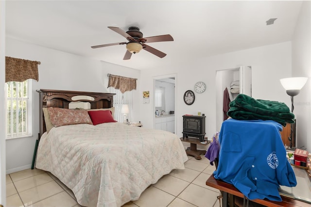 tiled bedroom with connected bathroom, a wood stove, and ceiling fan