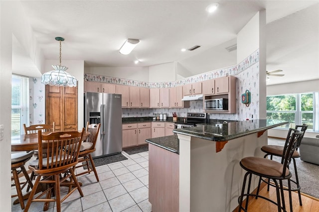 kitchen featuring light brown cabinets, stainless steel appliances, kitchen peninsula, dark stone counters, and pendant lighting