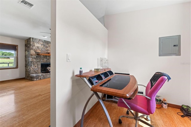 home office with electric panel, ceiling fan, a fireplace, and hardwood / wood-style flooring