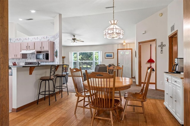 dining area with ceiling fan with notable chandelier, light hardwood / wood-style floors, and high vaulted ceiling