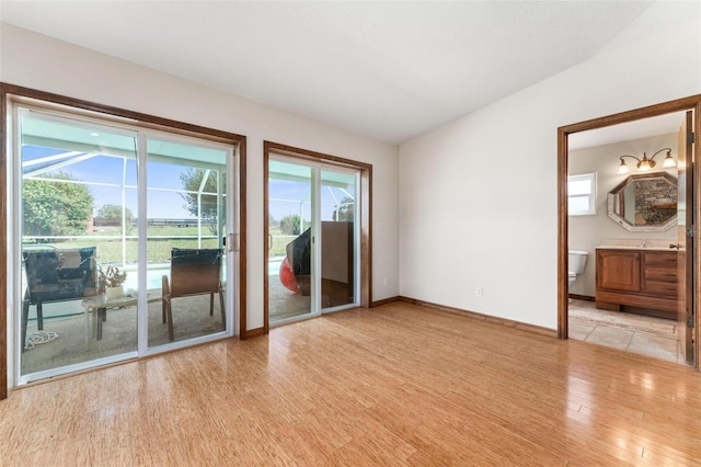 empty room with plenty of natural light, light wood-type flooring, and lofted ceiling