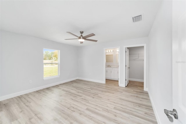 unfurnished bedroom with a walk in closet, light hardwood / wood-style flooring, a closet, connected bathroom, and ceiling fan