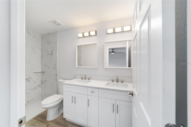 bathroom with toilet, a tile shower, ceiling fan, dual vanity, and hardwood / wood-style flooring