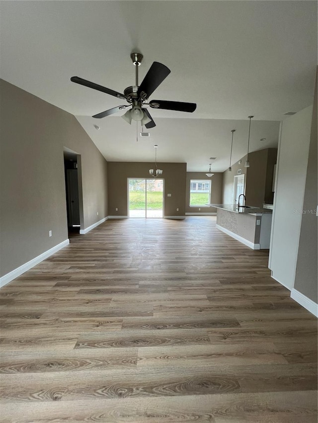 unfurnished living room with light wood-type flooring, ceiling fan with notable chandelier, and vaulted ceiling