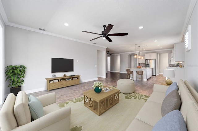 living room featuring hardwood / wood-style floors, ceiling fan with notable chandelier, and crown molding