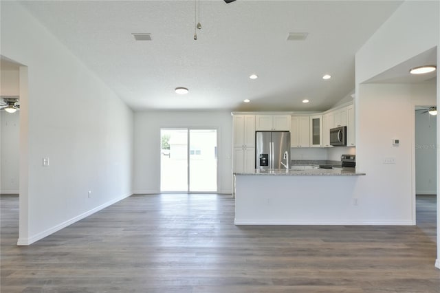 kitchen with appliances with stainless steel finishes, hardwood / wood-style floors, ceiling fan, and light stone countertops