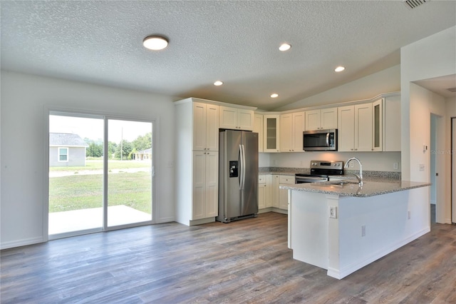 kitchen featuring light wood-type flooring, kitchen peninsula, light stone counters, appliances with stainless steel finishes, and lofted ceiling