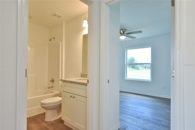 full bathroom featuring toilet, wood-type flooring, ceiling fan, washtub / shower combination, and vanity