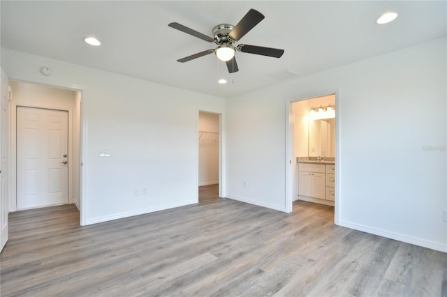 unfurnished bedroom featuring light hardwood / wood-style floors, a walk in closet, a closet, ceiling fan, and connected bathroom