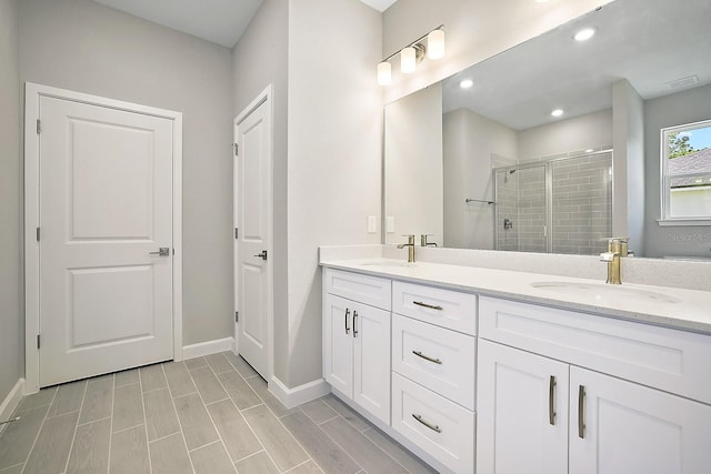 full bathroom featuring double vanity, a shower stall, baseboards, and a sink