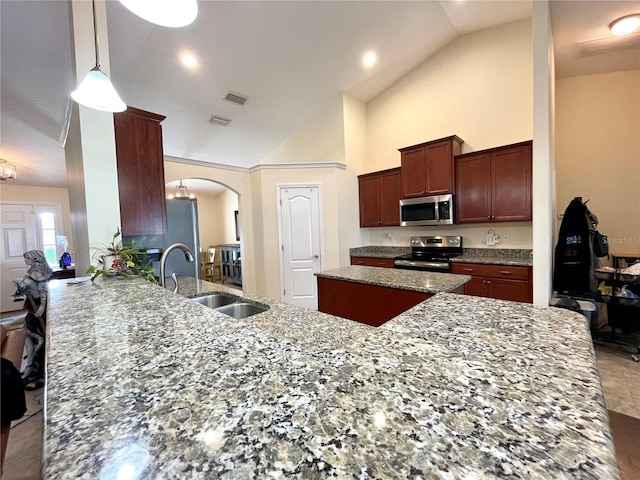 kitchen with high vaulted ceiling, decorative light fixtures, light stone counters, sink, and appliances with stainless steel finishes