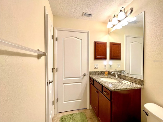 bathroom featuring vanity, toilet, tile patterned flooring, and a textured ceiling