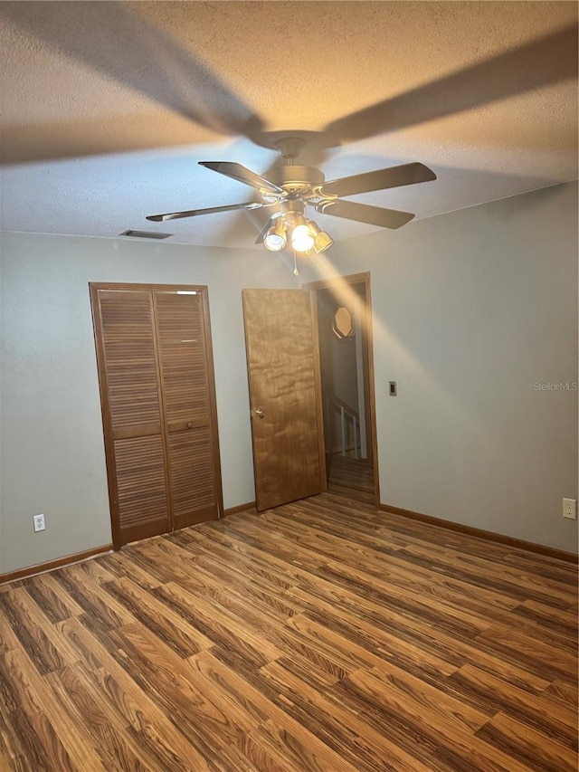 unfurnished bedroom featuring ceiling fan, visible vents, baseboards, a textured ceiling, and wood finished floors