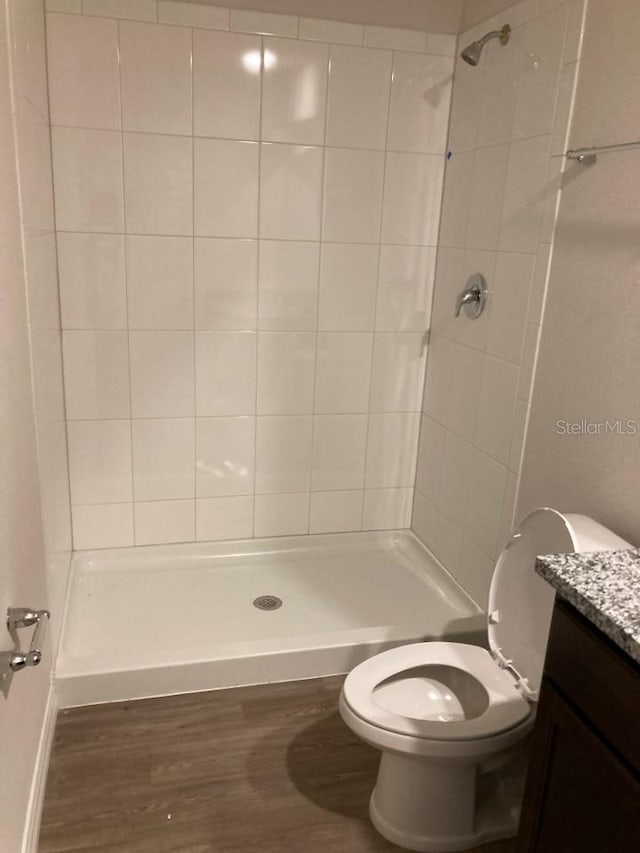 bathroom with vanity, toilet, a tile shower, and hardwood / wood-style floors