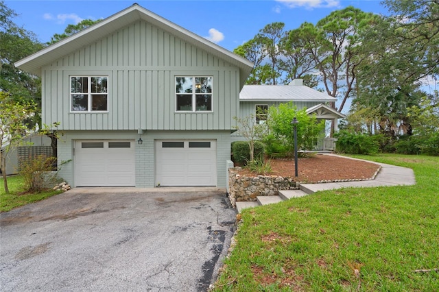 split level home featuring a front yard, a garage, brick siding, and board and batten siding