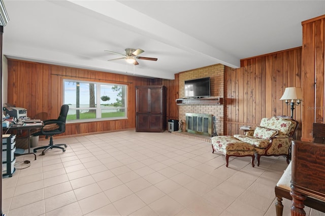 office with beamed ceiling, wooden walls, light tile patterned floors, a brick fireplace, and ceiling fan