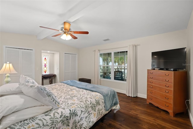 bedroom featuring visible vents, baseboards, lofted ceiling with beams, dark wood-type flooring, and two closets