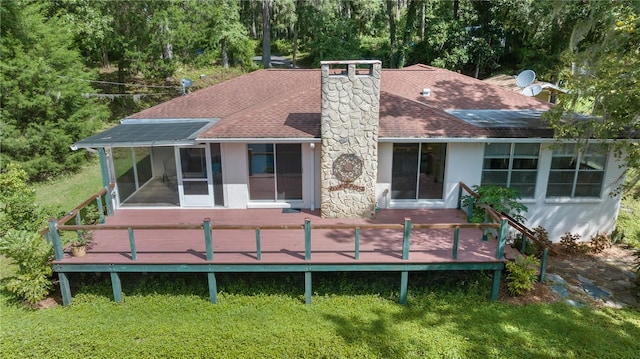 back of property with a wooden deck, a sunroom, and a lawn