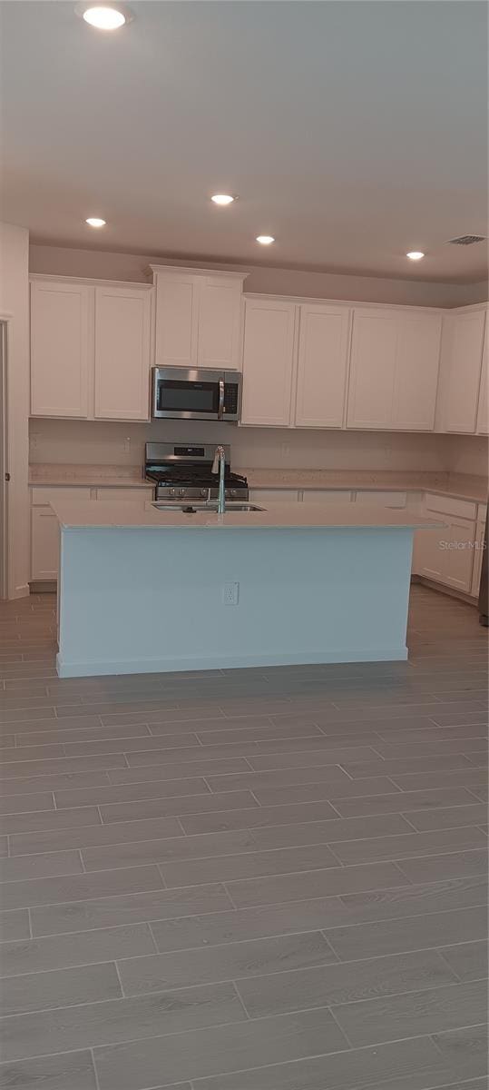 kitchen with an island with sink, stainless steel appliances, sink, and white cabinetry