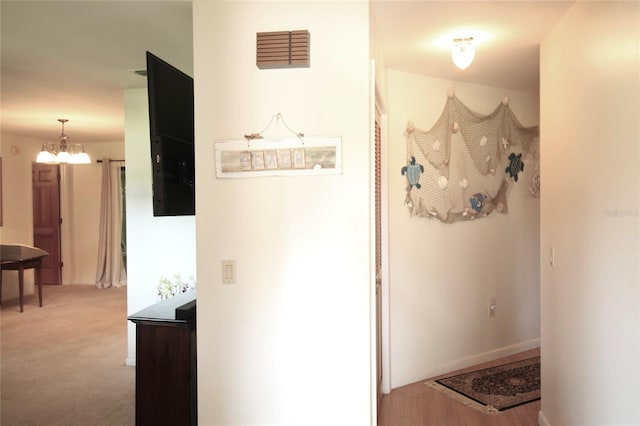 hall with light carpet and a chandelier