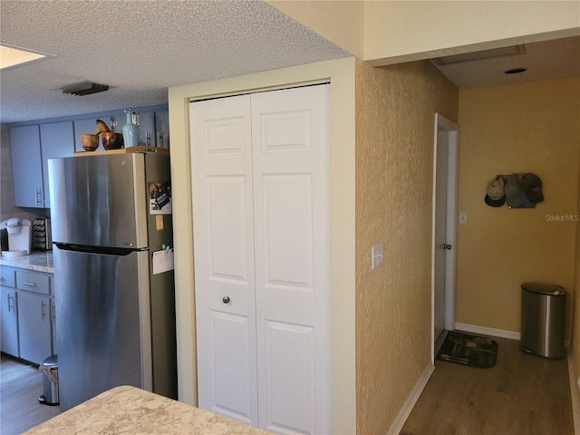 kitchen featuring hardwood / wood-style floors, a textured ceiling, and stainless steel refrigerator