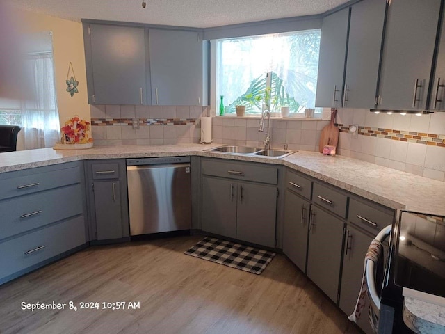 kitchen featuring sink, stainless steel dishwasher, gray cabinets, tasteful backsplash, and light hardwood / wood-style floors