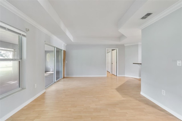 empty room featuring light wood-type flooring, a raised ceiling, and ornamental molding