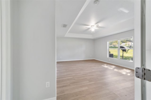 unfurnished room featuring a tray ceiling, ceiling fan, and light hardwood / wood-style floors