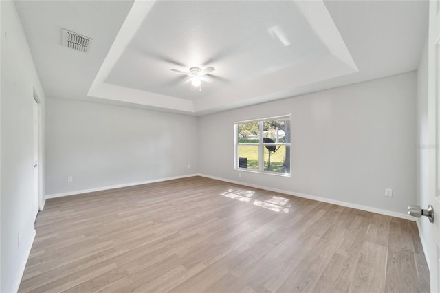 unfurnished room with light wood-type flooring, a raised ceiling, and ceiling fan