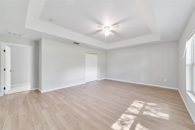 unfurnished room with a raised ceiling, ceiling fan, and light hardwood / wood-style floors