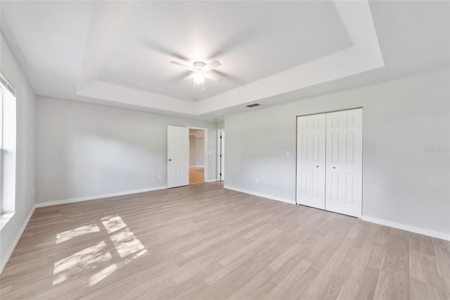 unfurnished bedroom with light hardwood / wood-style flooring, ceiling fan, a closet, and a tray ceiling