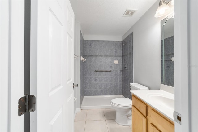 bathroom with tile patterned flooring, toilet, a tile shower, vanity, and a textured ceiling