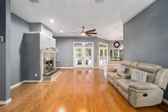 living room with a tiled fireplace, french doors, ceiling fan, and light hardwood / wood-style floors