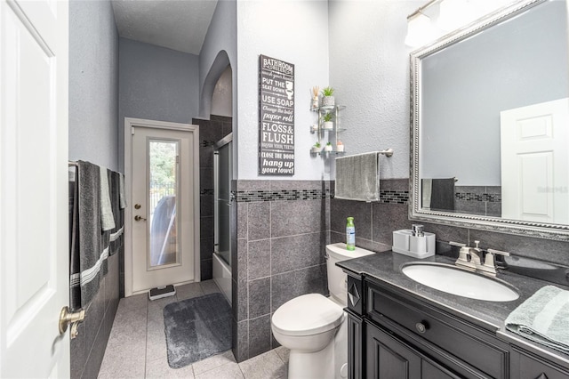 full bathroom with shower / bath combination with glass door, vanity, tile walls, toilet, and tile patterned floors