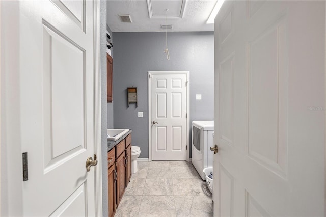 interior space featuring a textured ceiling, vanity, toilet, and washer / dryer