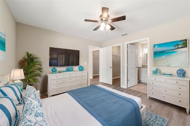 bedroom with ceiling fan, a spacious closet, ensuite bathroom, a closet, and light wood-type flooring