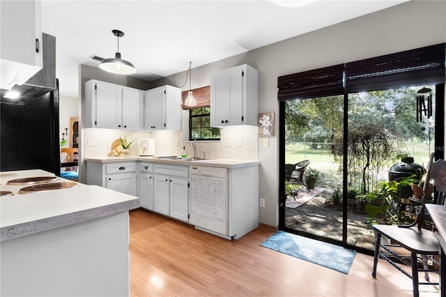 kitchen featuring white dishwasher, hanging light fixtures, light hardwood / wood-style floors, and white cabinetry