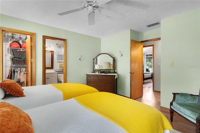 bedroom with ceiling fan, light hardwood / wood-style flooring, a walk in closet, a closet, and ensuite bath