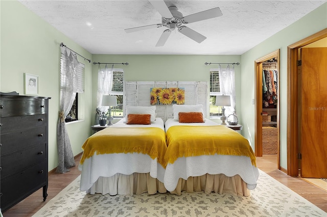 bedroom with ceiling fan, light hardwood / wood-style flooring, multiple windows, and a walk in closet