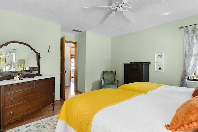 bedroom with a textured ceiling, ceiling fan, and light hardwood / wood-style flooring