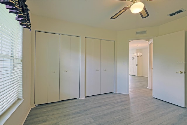 unfurnished bedroom featuring light hardwood / wood-style flooring, two closets, and ceiling fan with notable chandelier