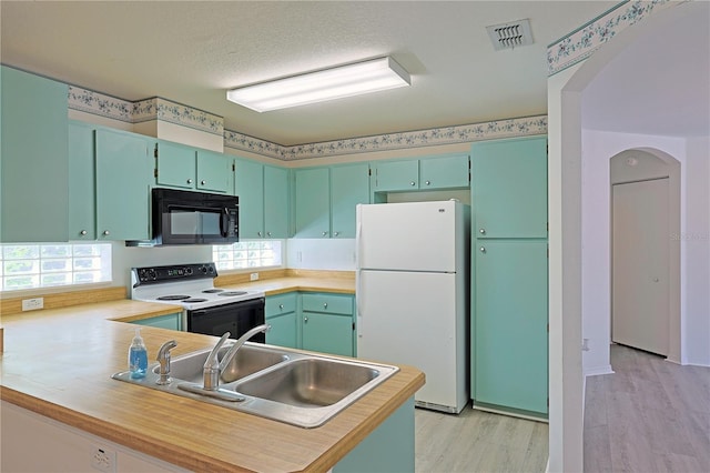 kitchen featuring white appliances, sink, light wood-type flooring, a textured ceiling, and kitchen peninsula