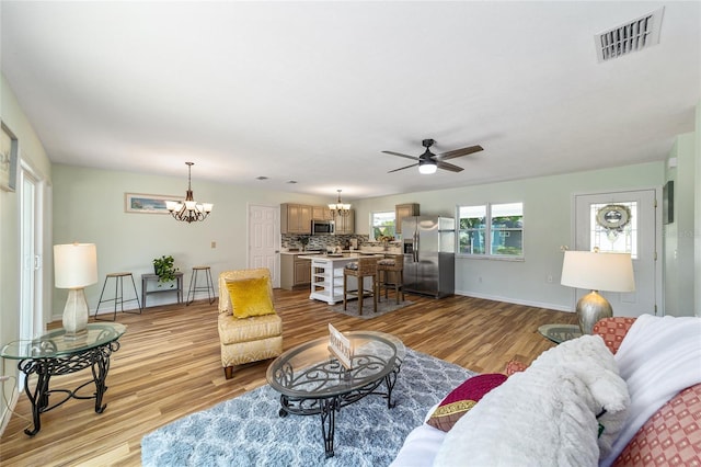 living area with a chandelier, ceiling fan, light wood-style floors, and baseboards