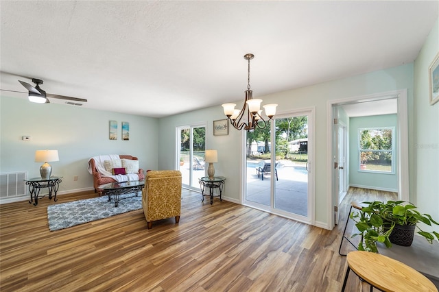 living room with ceiling fan with notable chandelier, wood-type flooring, and a textured ceiling