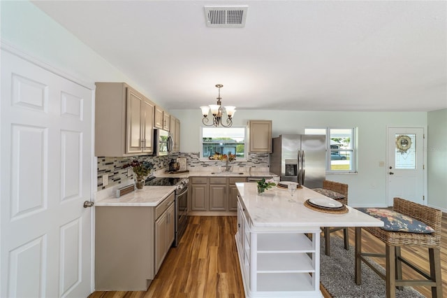 kitchen with an inviting chandelier, appliances with stainless steel finishes, light hardwood / wood-style floors, a center island, and sink