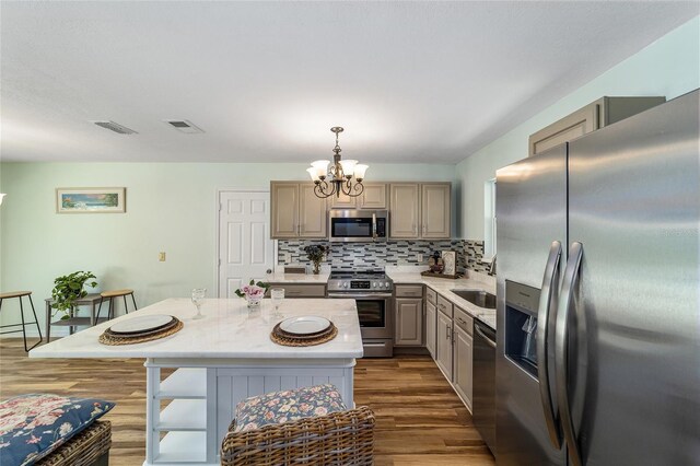 kitchen with appliances with stainless steel finishes, a chandelier, decorative backsplash, dark wood finished floors, and a center island