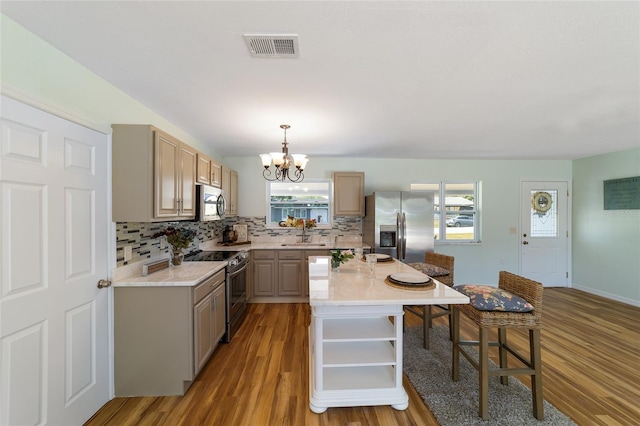 kitchen with stainless steel appliances, a chandelier, a kitchen breakfast bar, tasteful backsplash, and light countertops