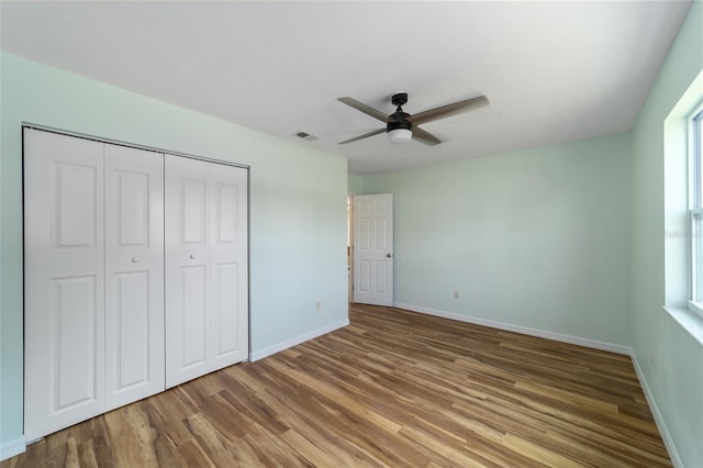 unfurnished bedroom featuring wood finished floors, a closet, baseboards, and ceiling fan