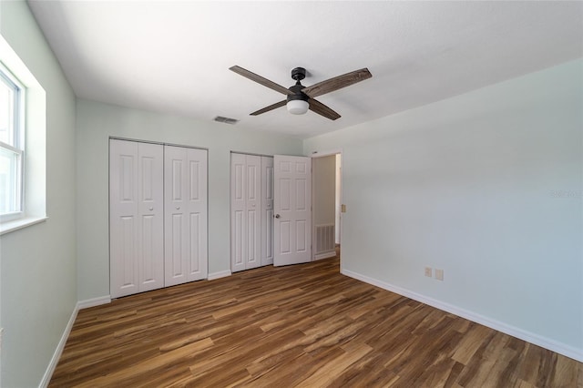 unfurnished bedroom featuring ceiling fan, dark hardwood / wood-style floors, and two closets